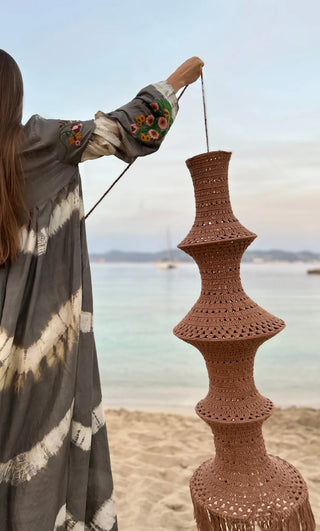 The Fisherman’s Lamp, Natural Colours: brown crochet pendant lamp held up by its cord on the beach
